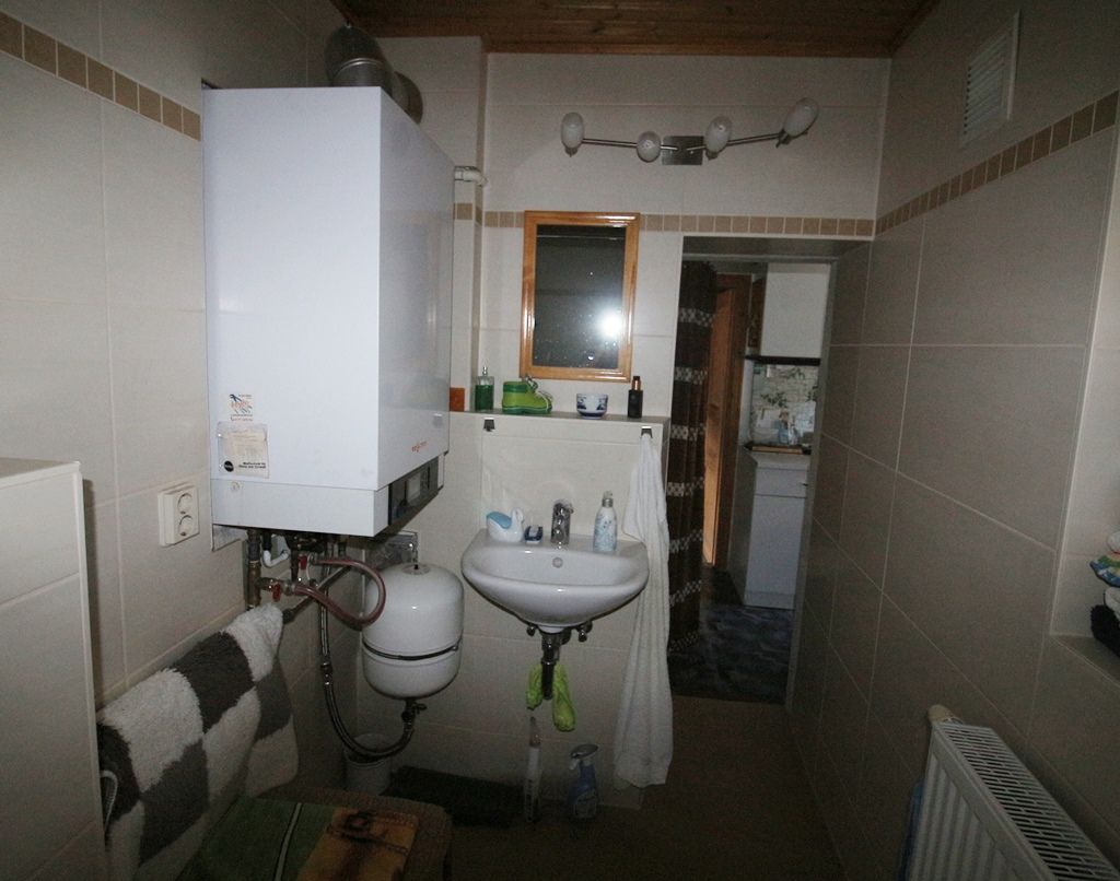 Kleines gefliestes Badezimmer mit wandmontiertem Boiler, Waschbecken, Spiegel und Heizkörper.