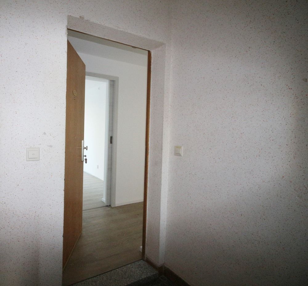 Offene Holztür in einem weißen Flur mit Holzboden und einer kleinen Stufe