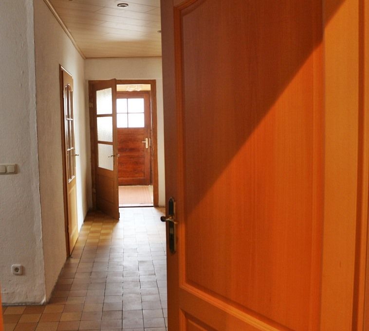 Holzflur mit offener Eingangstür, durch die helles Sonnenlicht hereinfällt
