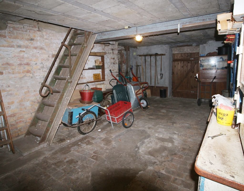 Keller mit Leiter, Fahrrädern, Regalen und Werkzeugen in einem Betonraum.