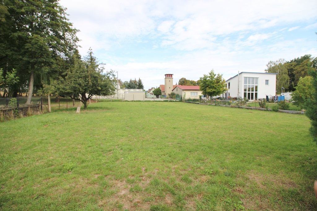 Offene, grasbewachsene Wiese mit Bäumen und einem weißen Haus unter einem teilweise bewölkten Himmel
