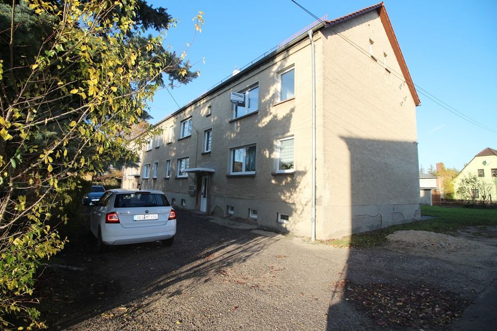 Mehrfamilienhaus mit daneben geparktem Auto auf einem Schotterplatz im hellen Sonnenlicht