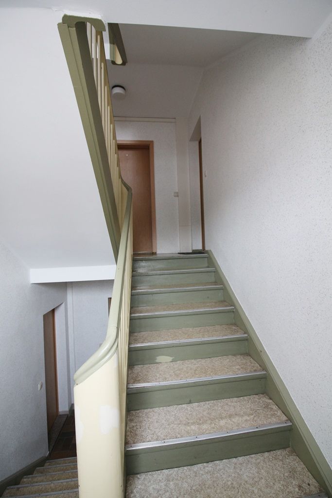 Steile Innentreppe mit grün gestreiftem Teppich und einer Tür am oberen Ende