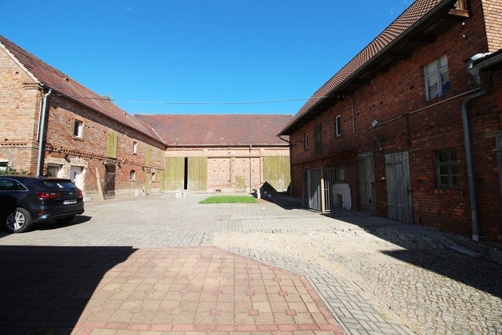 Sonniger Kopfsteinpflasterhof zwischen roten Backsteingebäuden mit geparkten Autos und einem großen Tor in der Ferne