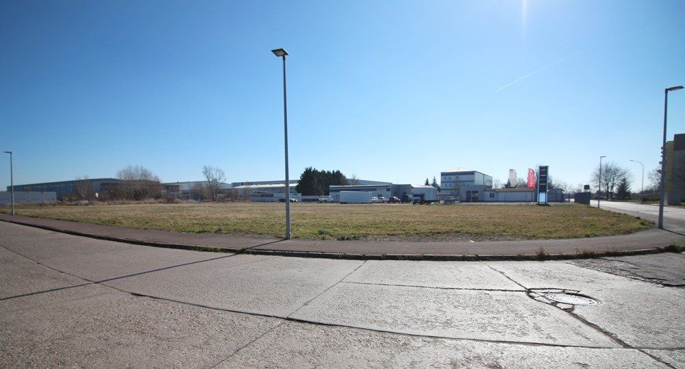 Ein leerer Parkplatz unter klarem, blauem Himmel, in der Ferne Gebäude.