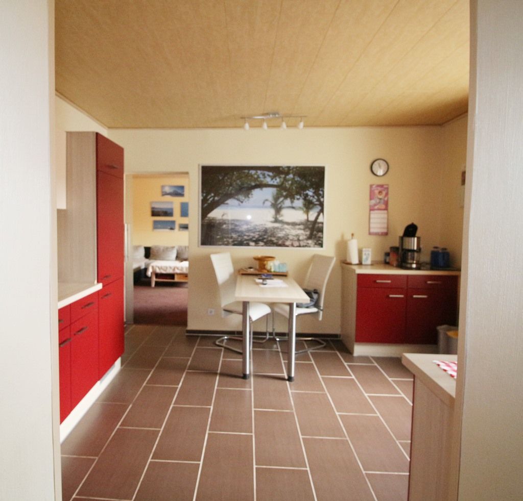 Moderne Wohnküche mit roten Schränken, weißem Tisch und großem Wandbild.