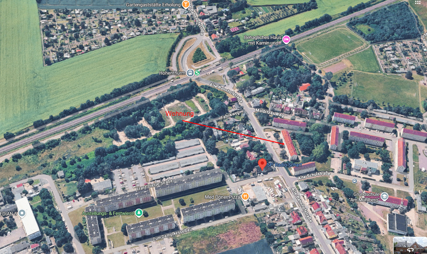 Luftaufnahme einer Stadtkreuzung mit Häusern, Straßen, geparkten Autos und nahegelegenen grünen Feldern.