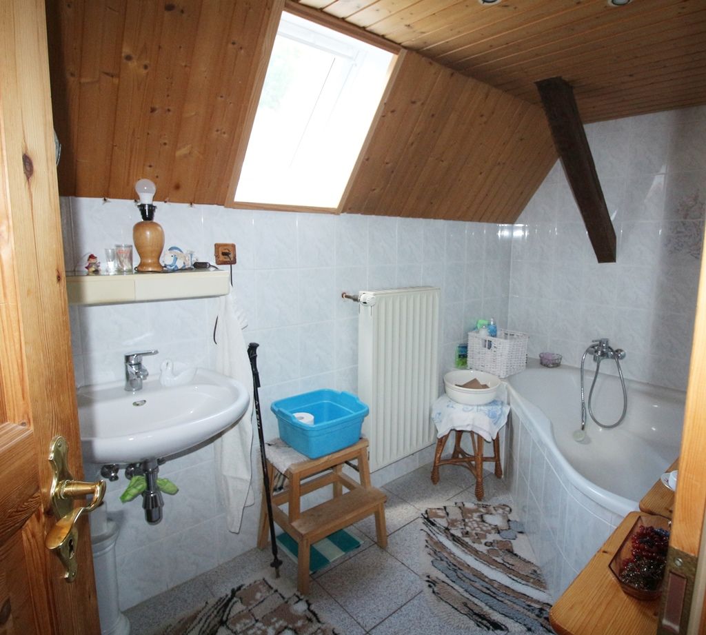 Kleines Dachgeschossbad mit Waschbecken, Toilette, Badewanne, Dachfenster und gemusterten Teppichen