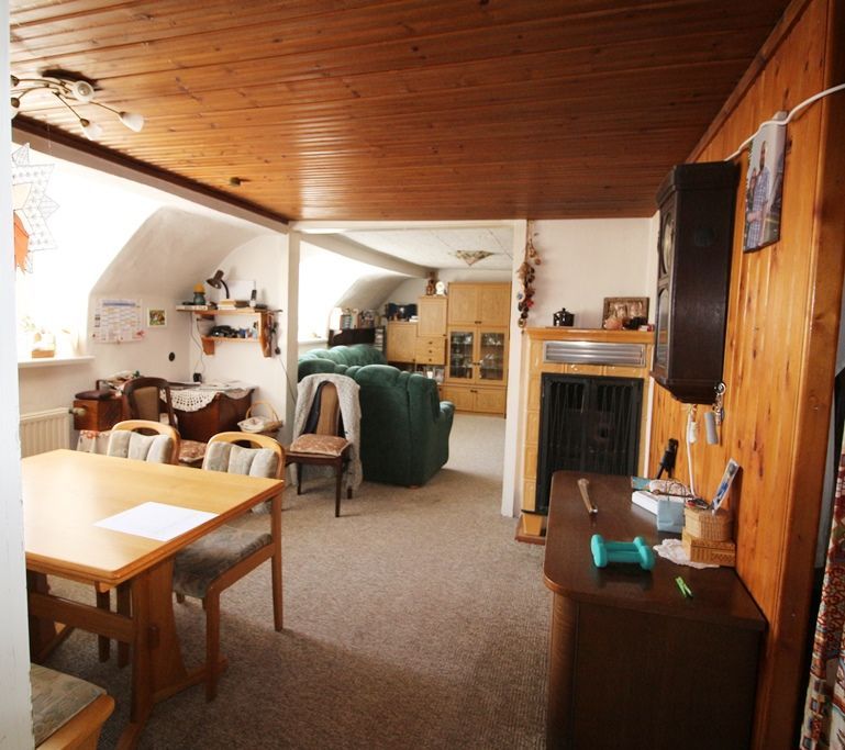 Gemütliches, holzgetäfeltes Wohnzimmer mit Esstisch, grünem Sofa und Schränken unter einer Dachschräge