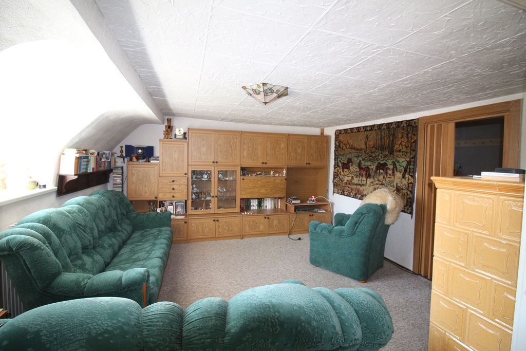 Wohnzimmer mit grünen Sofas, Holzschränken, Teppichboden und einer schrägen weißen Decke