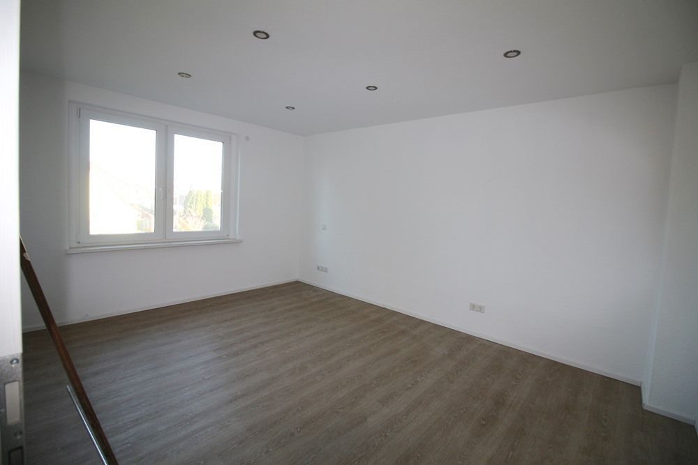Leerer weißer Raum mit Holzboden, Einbaustrahlern und einem Fenster auf der linken Seite.