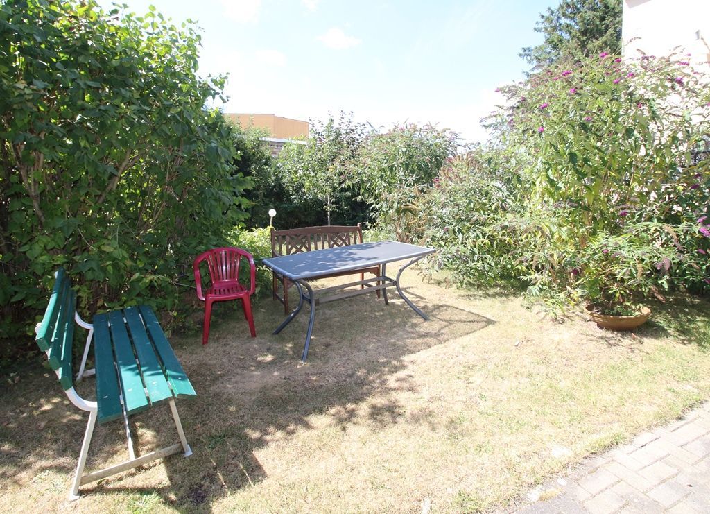 Hinterhofgarten mit grüner Bank, rosa Stuhl, Tisch und Büschen im Sonnenlicht