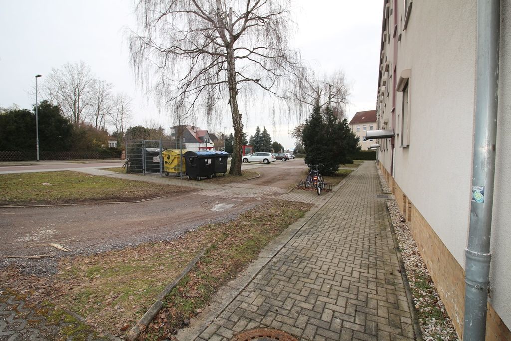 Ein leerer Backsteinpflasterweg neben einem Gebäude, daneben eine Straße und Mülltonnen an einem bewölkten Tag
