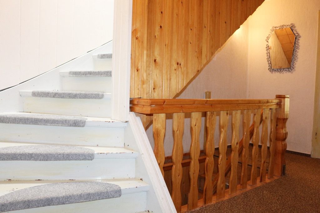 Weiße Treppe neben einem holzgetäfelten Flur mit kleinem Wandspiegel und Teppichboden im Treppenabsatz.