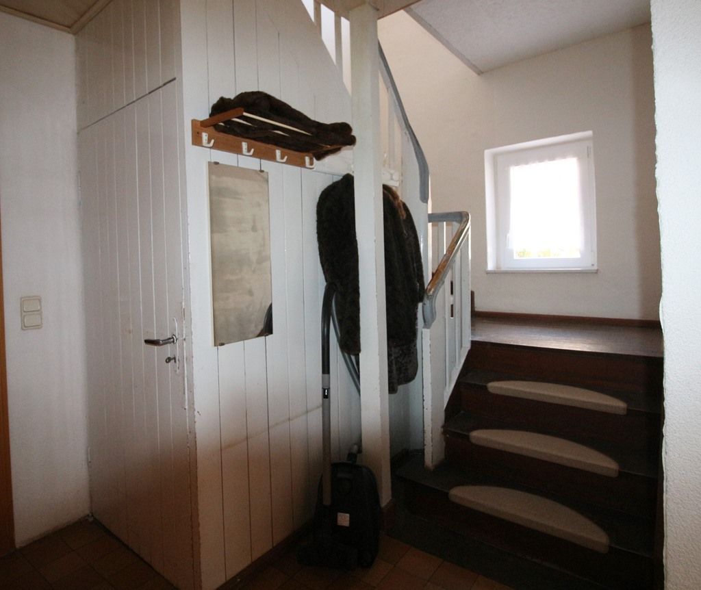 Eingangsbereich mit Treppe, Garderobe und einem kleinen Fenster an einer weißen Wand