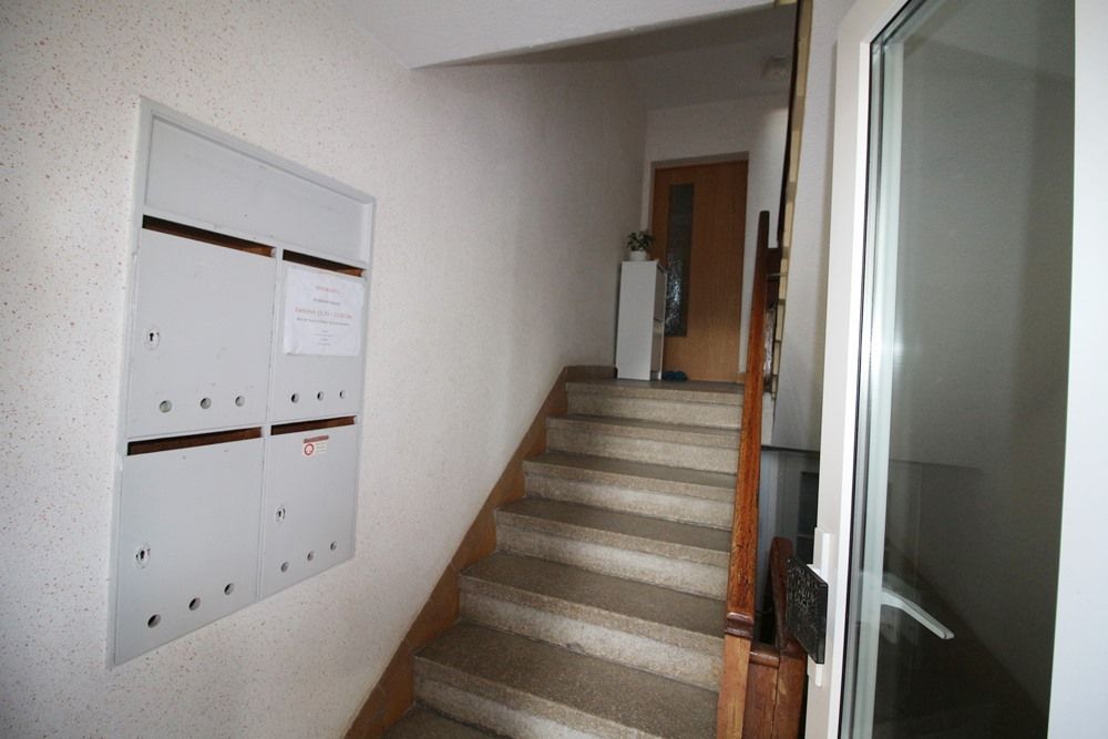 Innentreppenhaus mit Briefkästen auf der linken Seite und einer Glastür auf der rechten Seite.