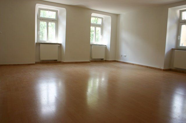 Leerer Raum mit Holzboden und drei hohen Fenstern, die Tageslicht hereinlassen