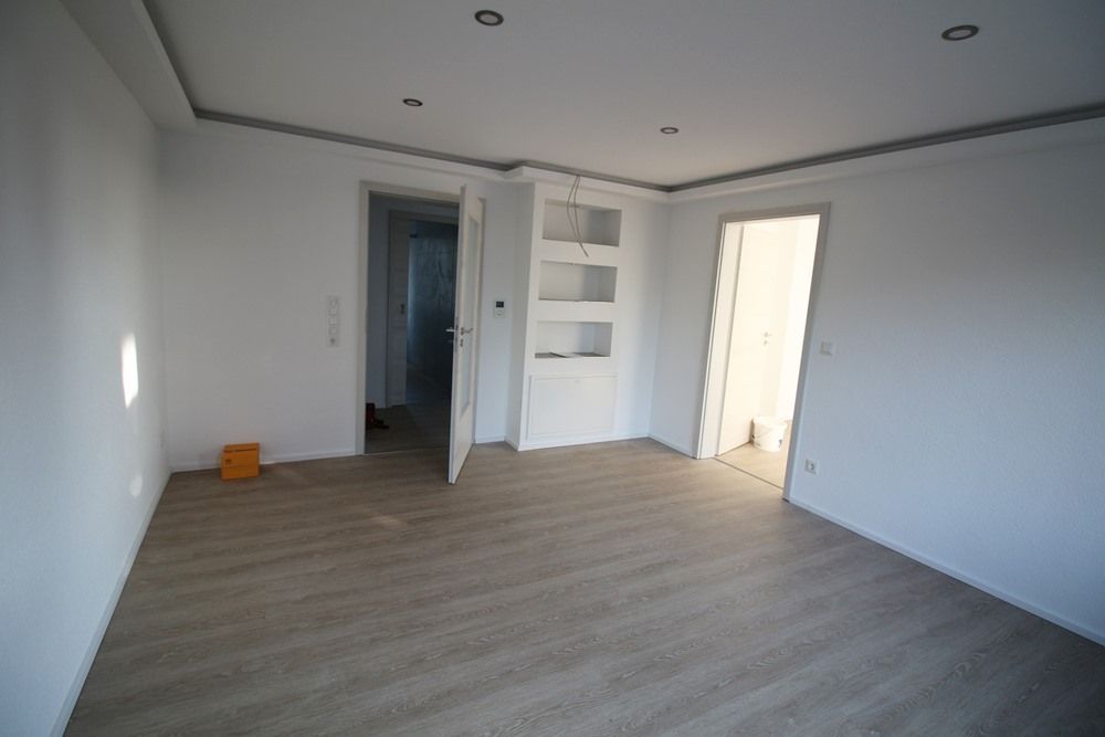 Leeres weißes Zimmer mit grauem Holzboden, Einbaustrahlern und eingebauten Regalen.