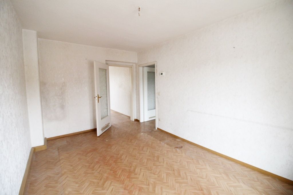 Leerer weißer Raum mit Parkettboden und offenen Türen zu einem Flur und einem weiteren Raum