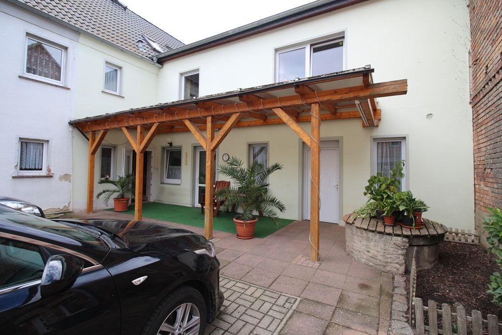 Hausinnenhof mit hölzerner Pergola, Topfpflanzen und einem geparkten schwarzen Auto vor weißen Wänden
