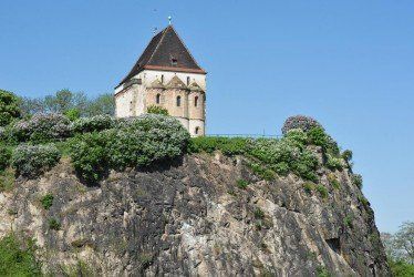 Kleiner Steinturm auf einer Felsklippe, umgeben von Grün unter klarem, blauem Himmel
