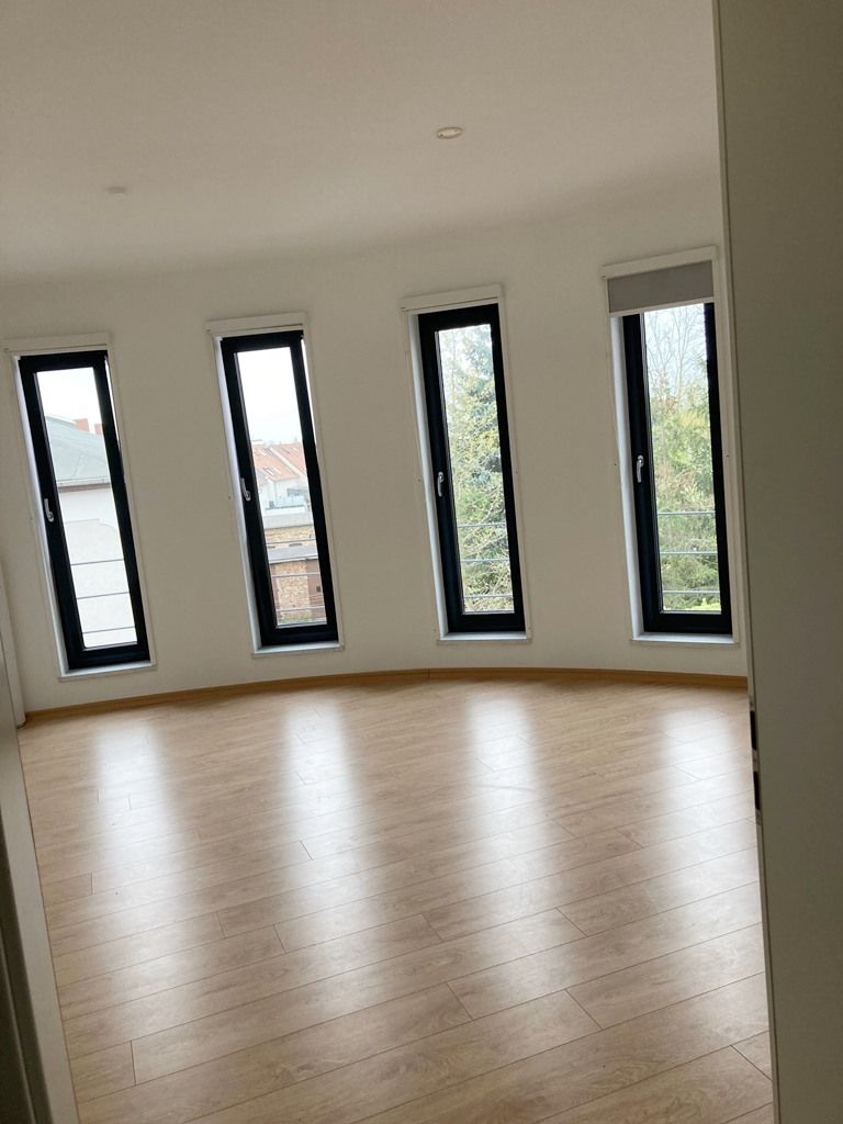 Leeres, modernes Zimmer mit hellem Holzboden, geschwungener Wand und hohen, schmalen Fenstern mit Blick ins Grüne