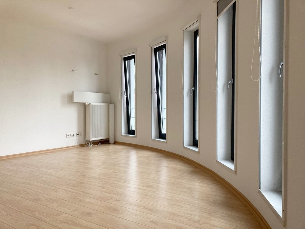 Leerer, moderner Raum mit geschwungenem Holzboden und hohen Fenstern entlang einer Wand