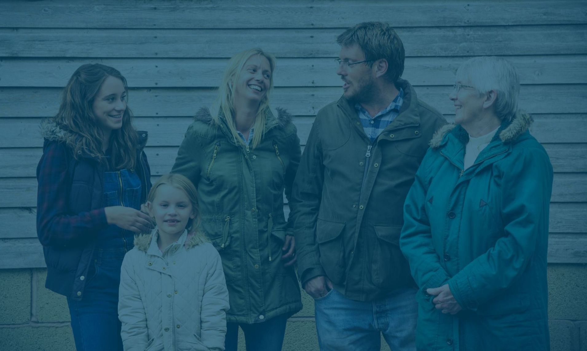 A group of people standing next to each other in front of a wooden wall.