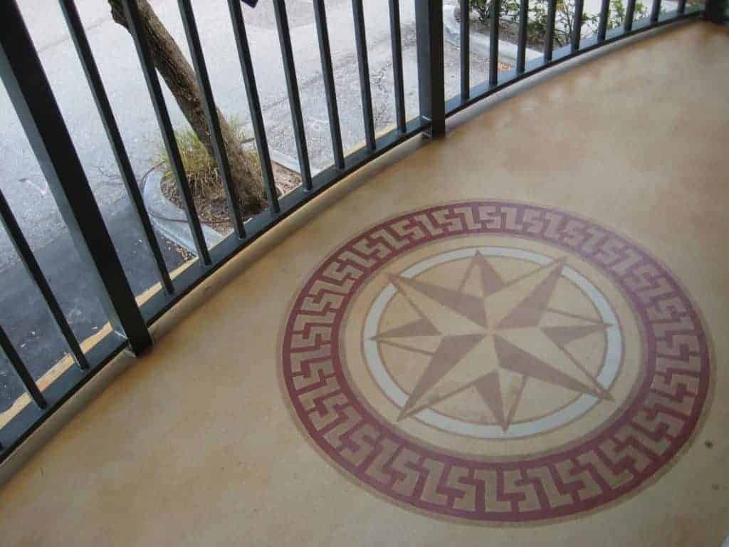 Decorative compass rose mosaic on a patio beside a black metal railing, overlooking wet pavement
