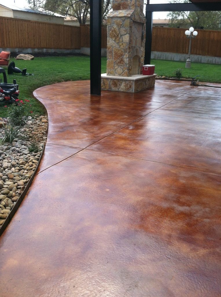 Stamped concrete patio with a stone pillar, wet from rain, in a fenced backyard.