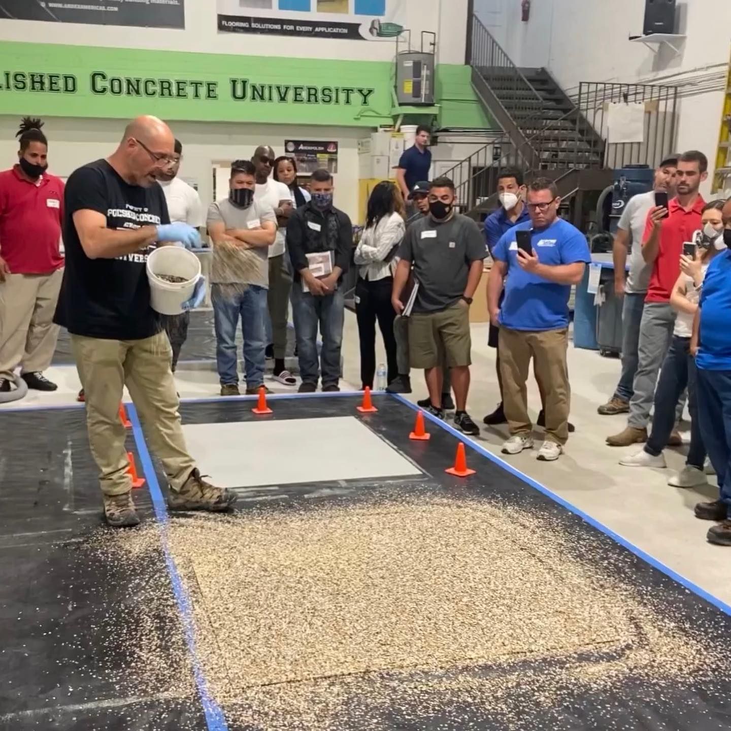 People watching a concrete testing demo with a man smoothing wet concrete between orange cones.