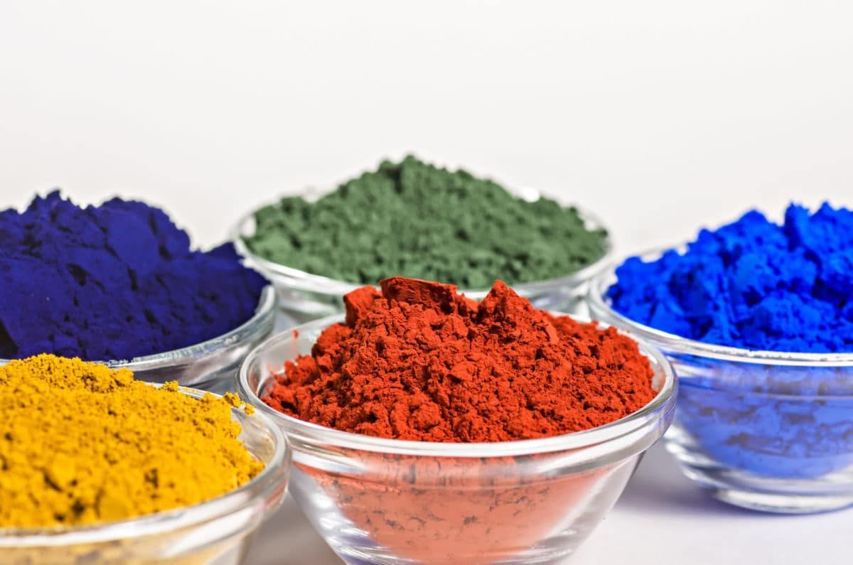 Bowls of brightly colored powder pigments in yellow, purple, green, red, and blue