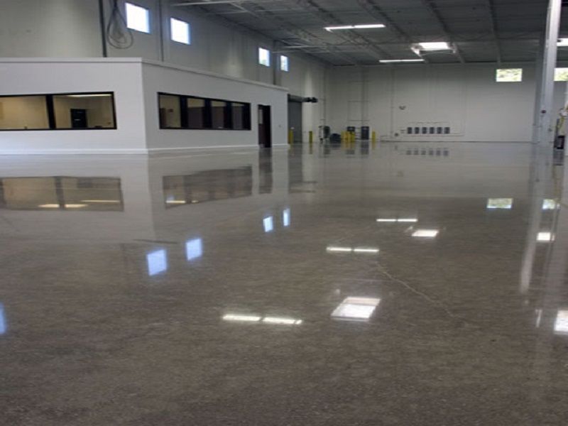 Empty polished warehouse interior with glossy reflective floor and high windows on gray walls