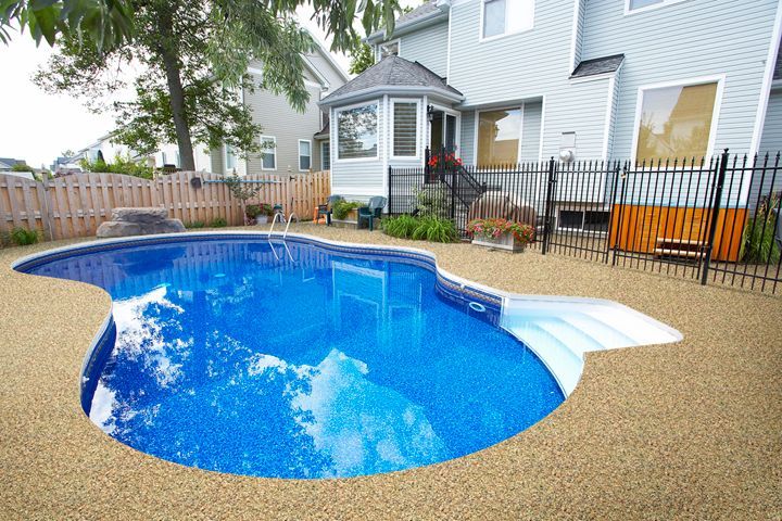 Backyard patio with a small blue pool, tan deck, and house with outdoor seating and black fence