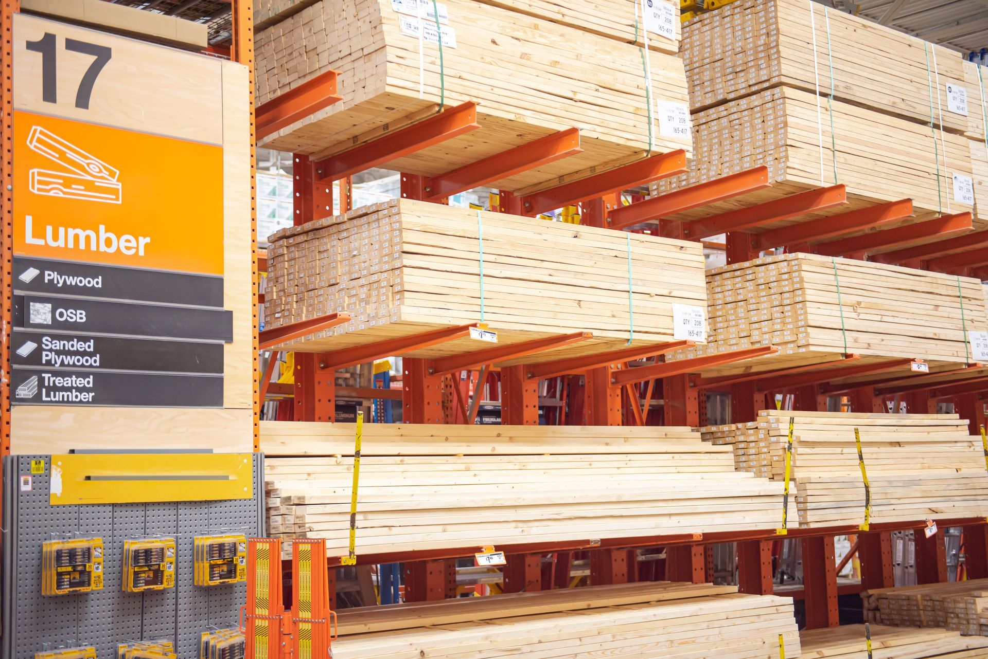 A Home Depot aisle sign labeled 17 Lumber with shelves of stacked wood panels and lumber boards.