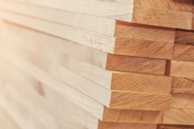 A stack of light-colored, sawn wooden planks arranged in neat horizontal layers. A stack of light-colored, sawn wooden planks arranged in neat horizontal layers.