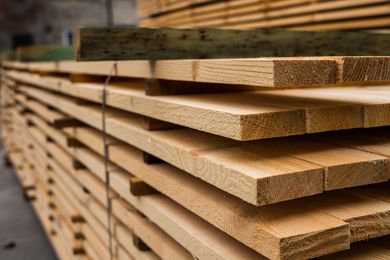 A large stack of light-colored, rough-cut lumber boards stored in a warehouse. A large stack of light-colored, rough-cut lumber boards stored in a warehouse.