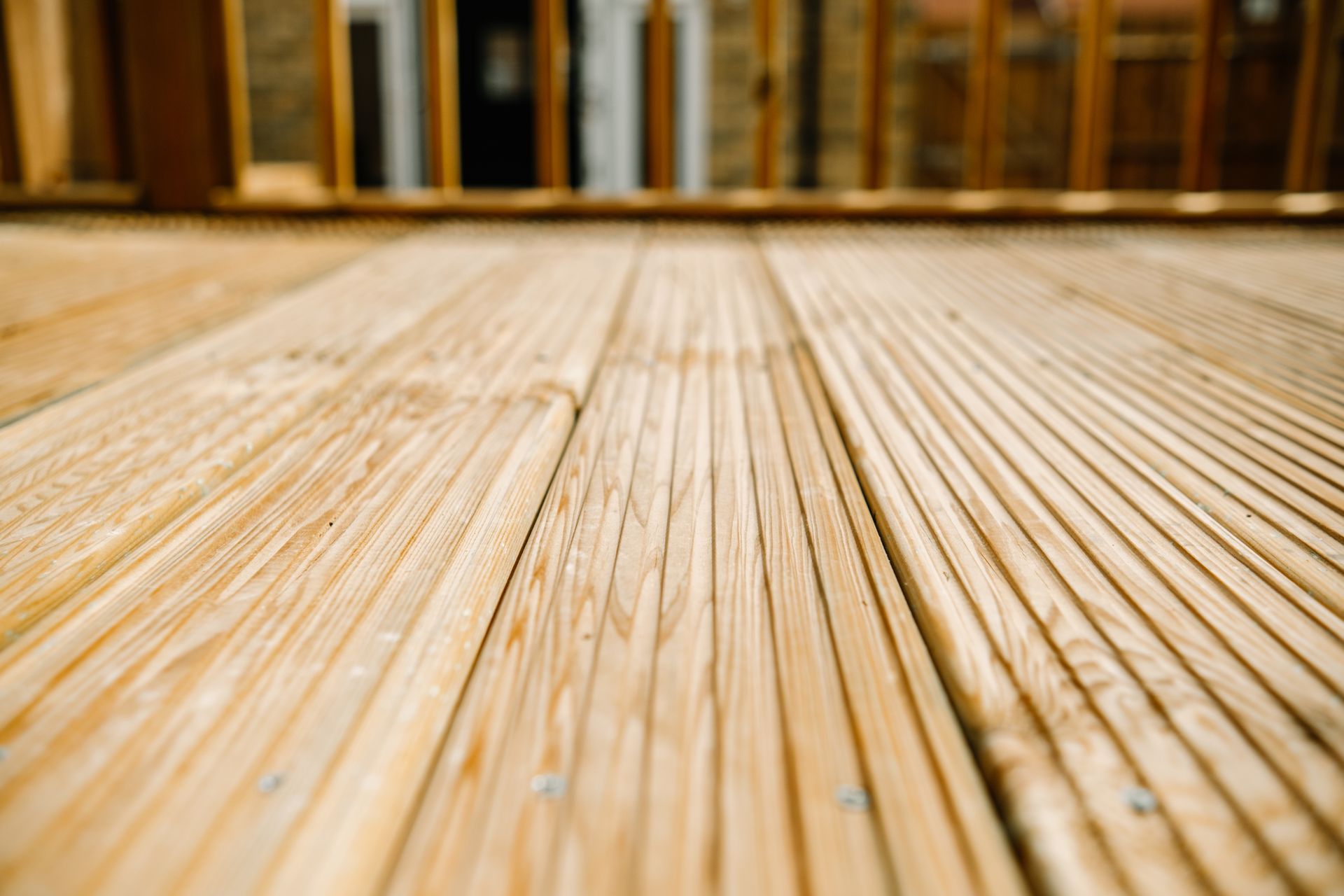 Close-up, low-angle view of light-colored, grooved wooden deck boards extending toward a wooden railing in the background.