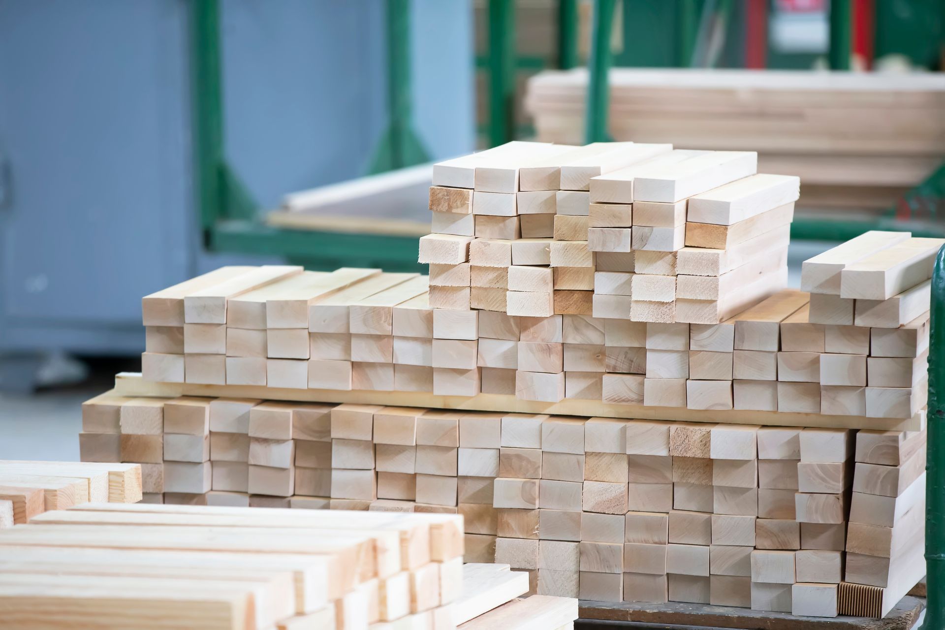 A stack of light-colored wooden beams neatly organized in a workshop or industrial storage setting.