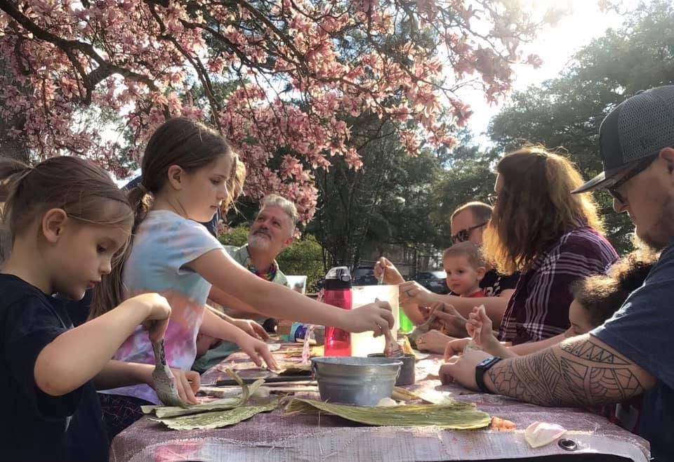 Family gathered outdoors around a table, sharing food and drinks under blooming trees.