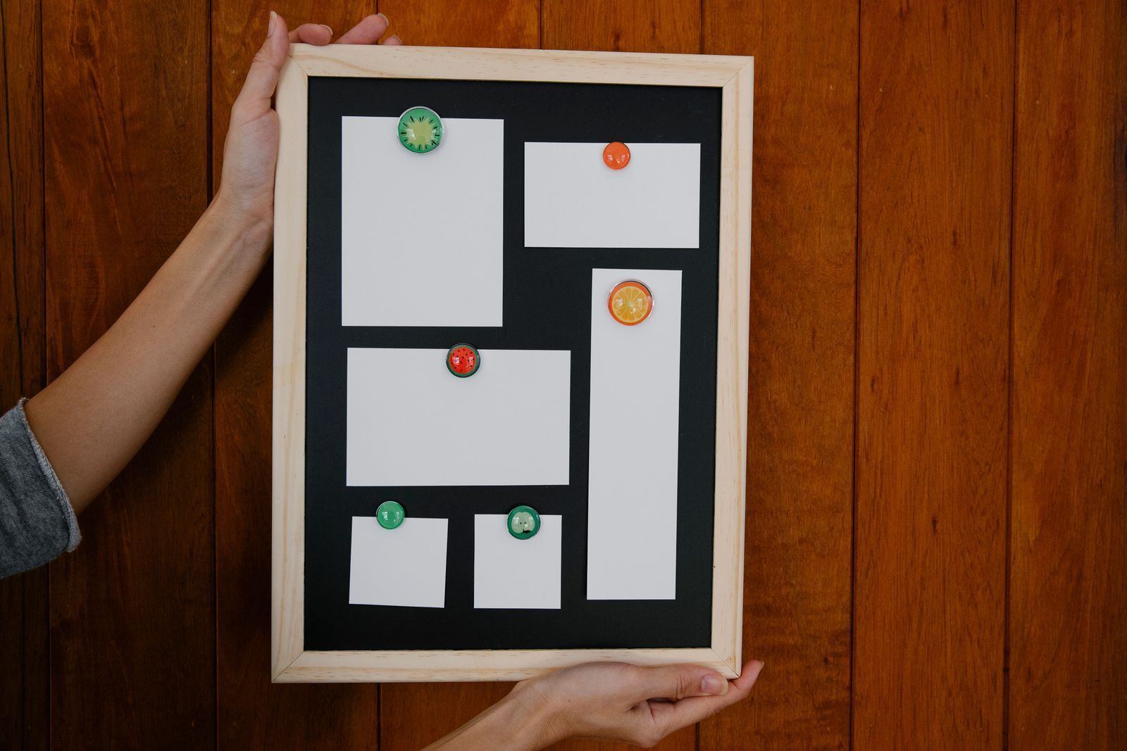Hands holding a framed abstract black-and-white geometric collage with colored pushpins.