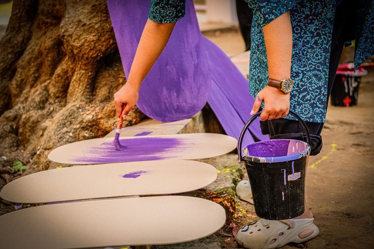 Person painting large oval shapes white and purple on the ground with a bucket and brush outdoors