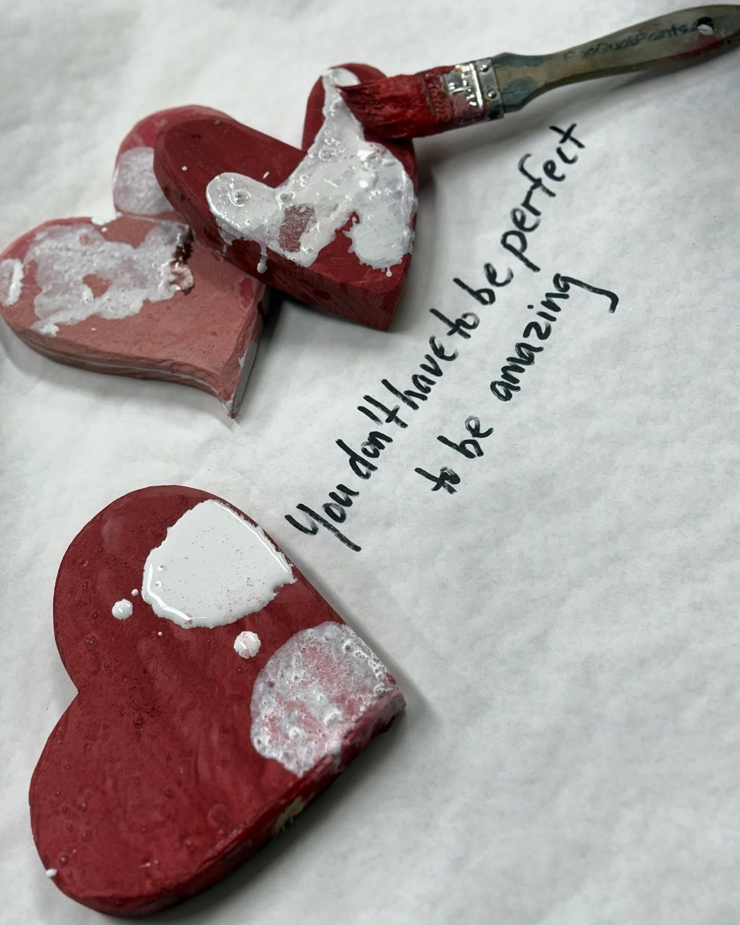 Three red heart-shaped painted wooden pieces with silver accents and a handwritten quote beside them.