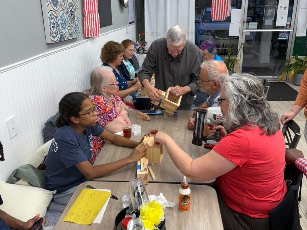 People seated around a table making crafts in a bright room with American flags on the wall