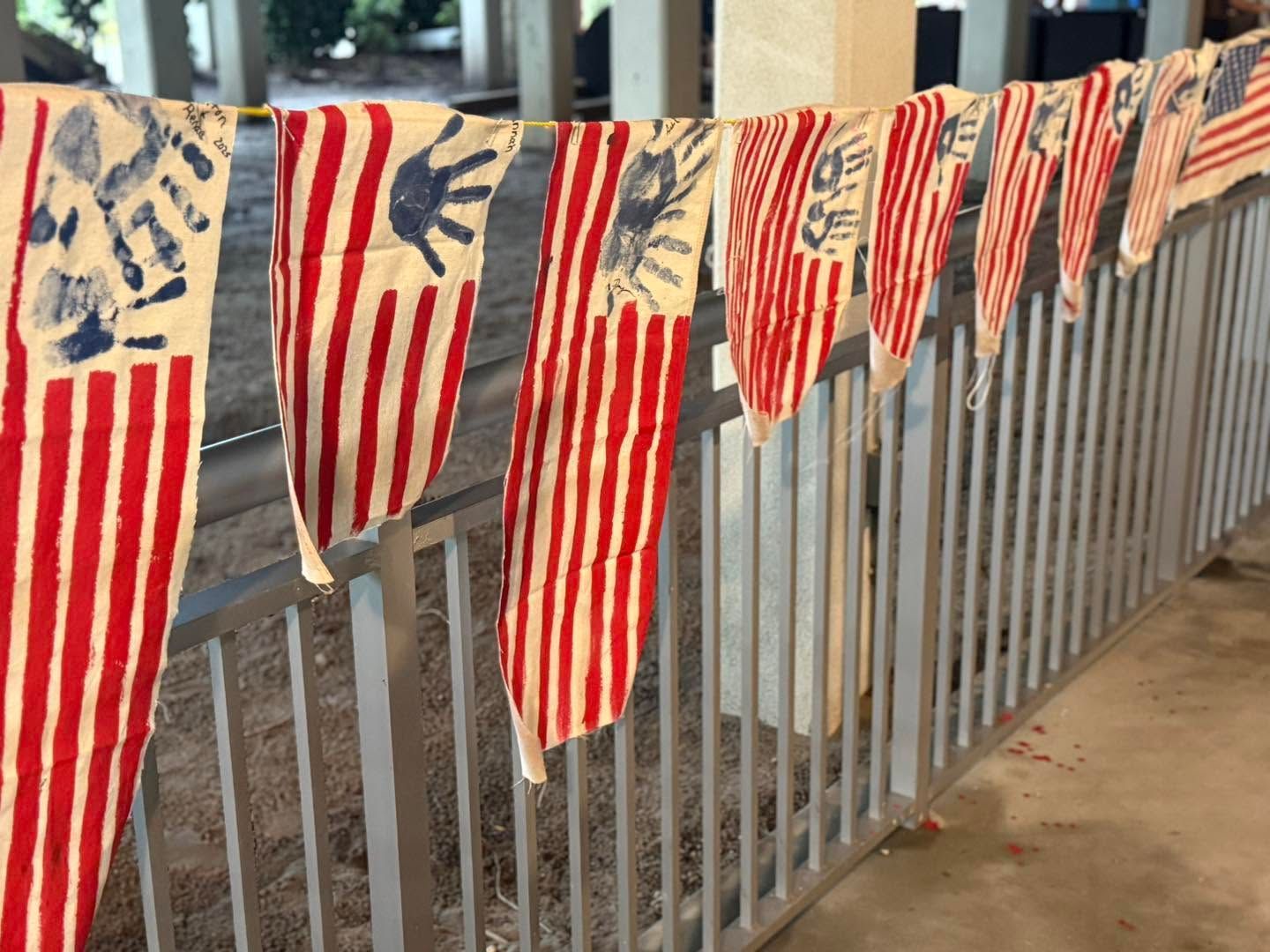 Patriotic red, white, and blue striped banners hung along a metal fence outdoors.