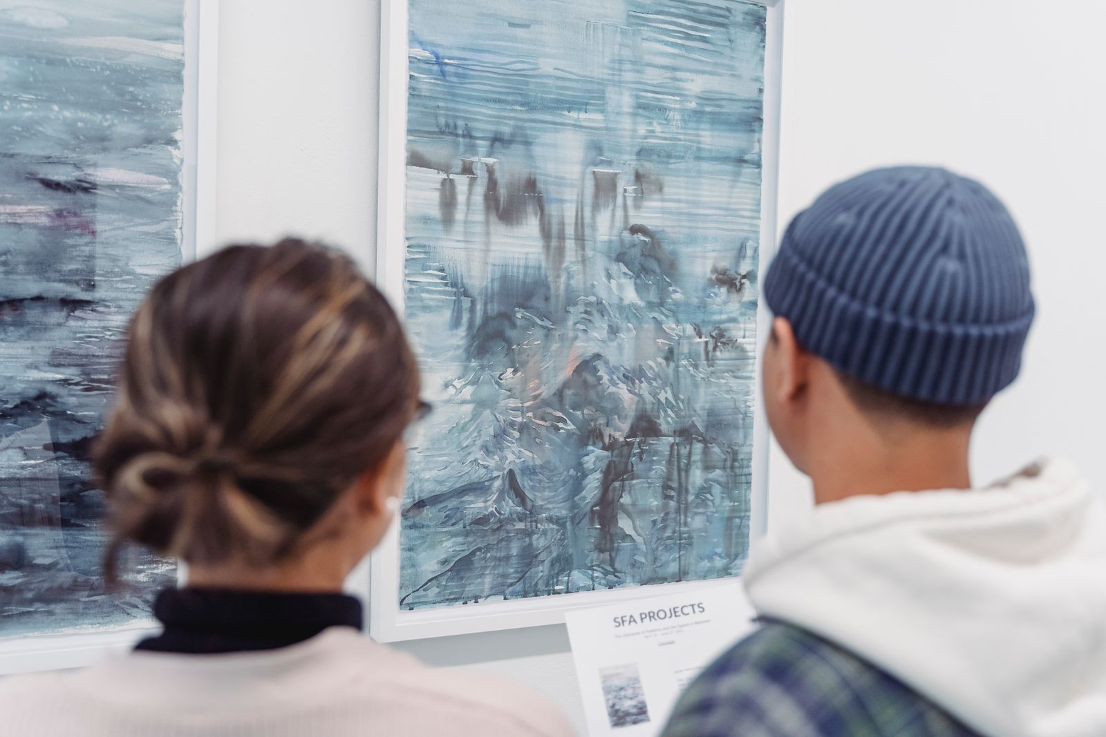 Two people viewing abstract blue paintings in a gallery