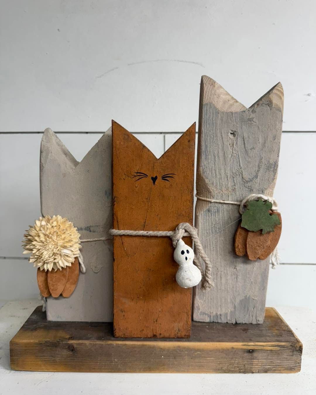 Three rustic cat-shaped wooden ornaments with flowers and a small white bunny on a base.