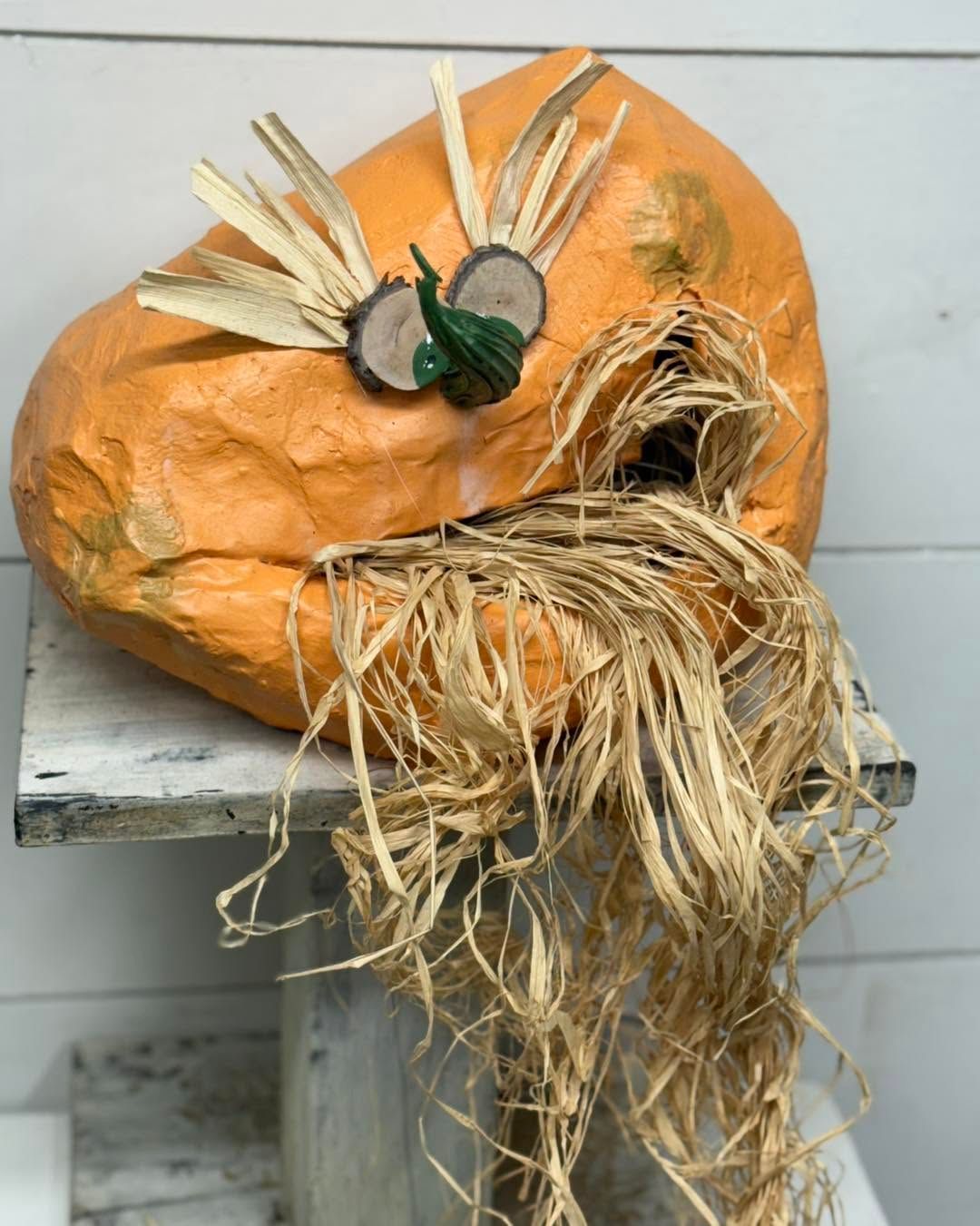 Orange pumpkin decoration with straw hair and small green eyes on a tiled bench
