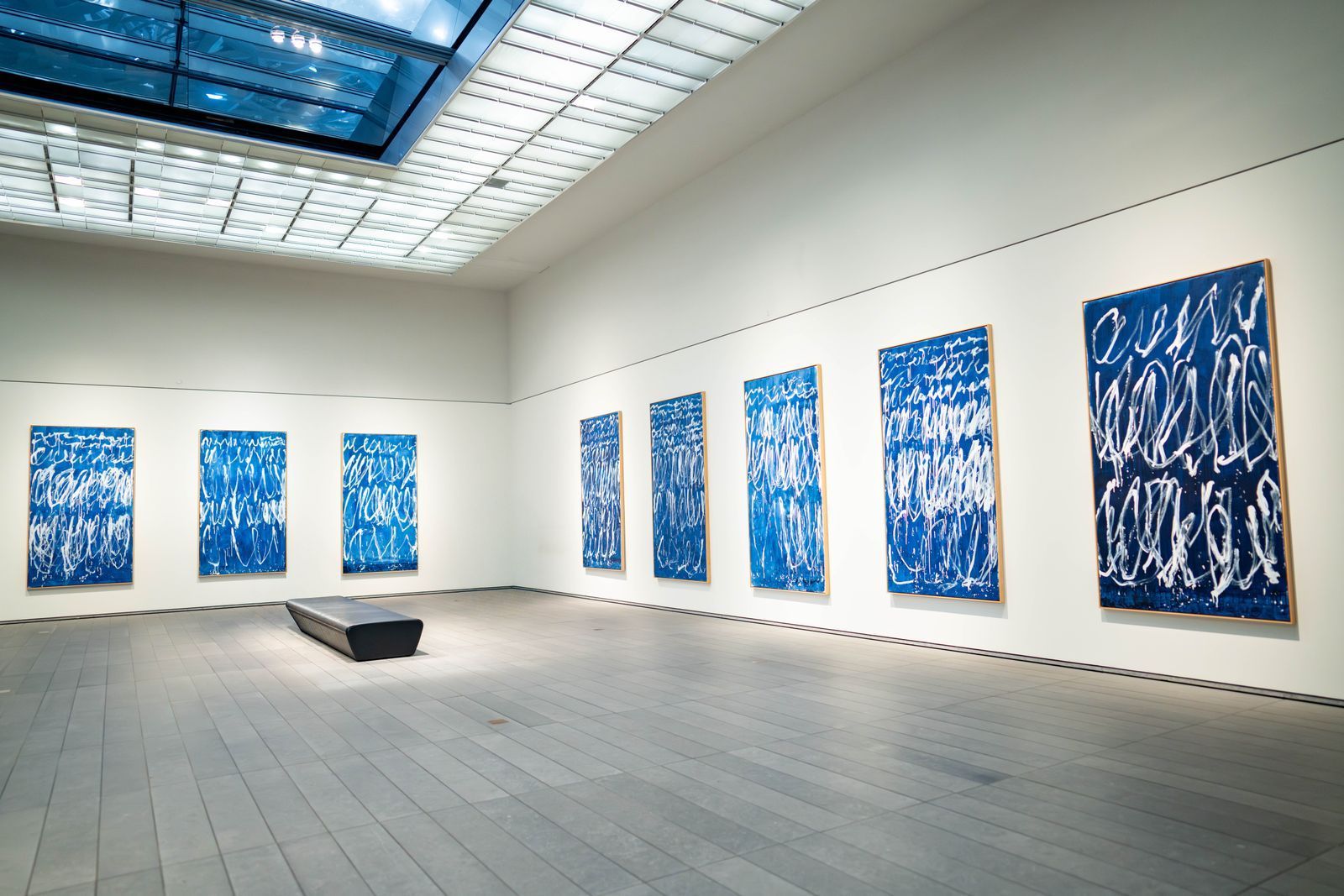 Modern art gallery with blue abstract paintings on white walls and a bench on a tiled floor