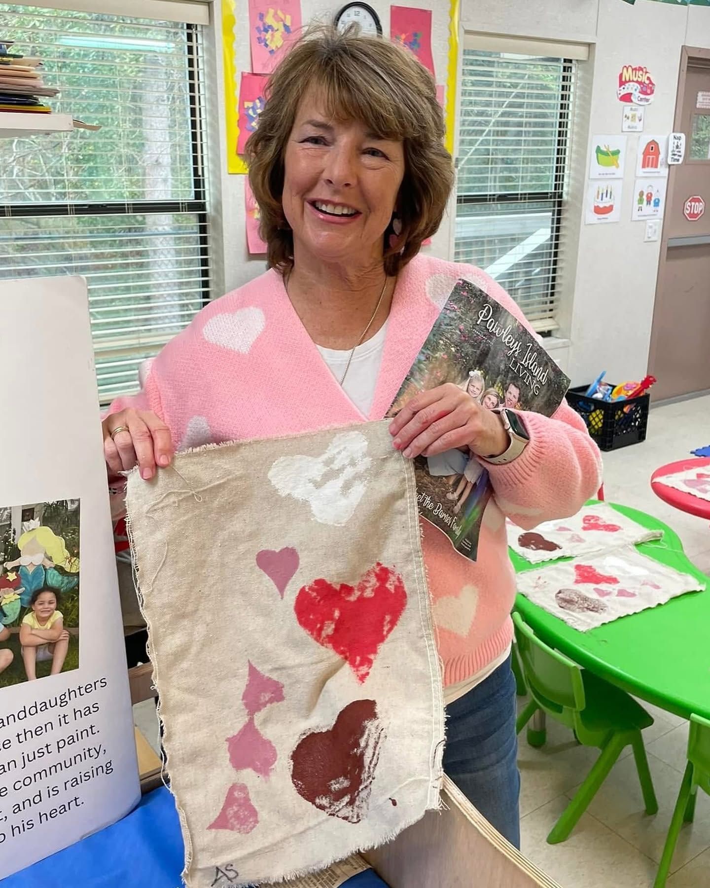 Woman in pink sweater holding a painted tote bag with heart designs in a classroom